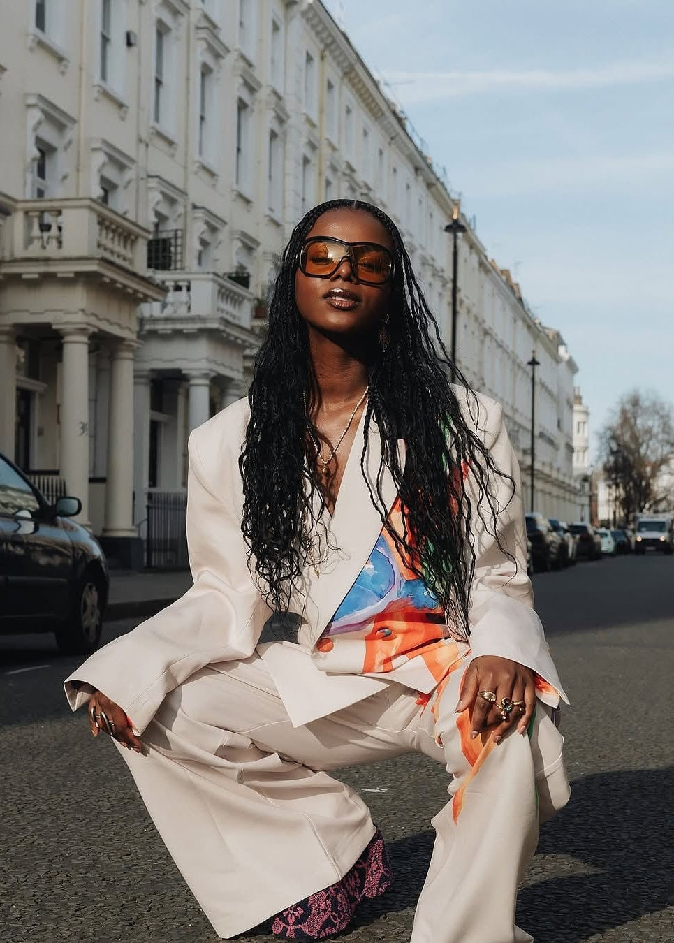 Woman in a stylish outfit sitting on a street with classic buildings in the background