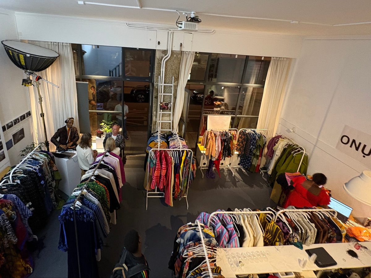 A high-angle view of a clothing boutique interior with multiple racks of garments, people browsing, and a visible ONULI sign on the wall.